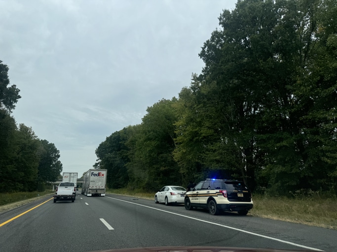 Police vehicle assisting a traffic incident on a highway in Nashville, TN surrounded by trees and vehicles during overcast weather